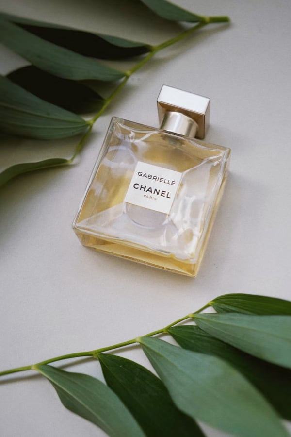 A perfume bottle with an amber colored liquid written Gabrielle Chanel Paris and with leaves around it