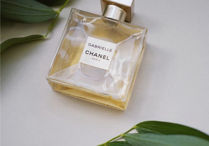 A perfume bottle with an amber colored liquid written Gabrielle Chanel Paris and with leaves around it